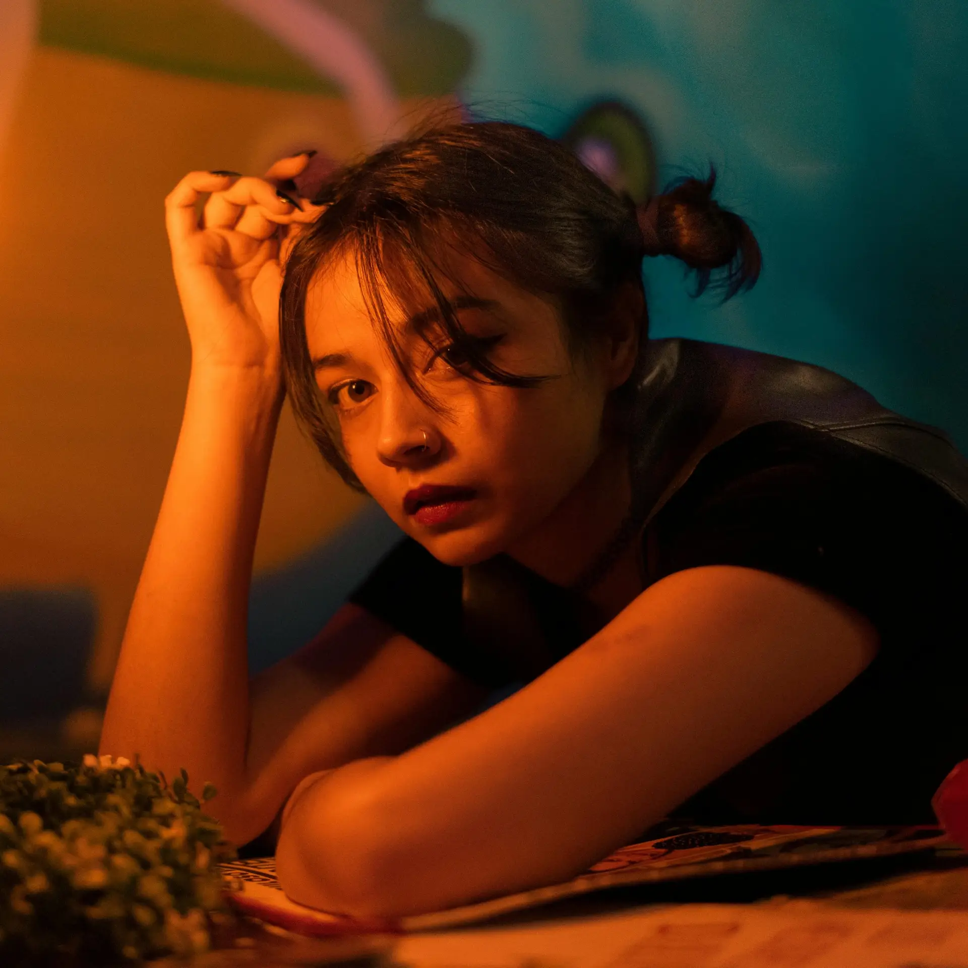 A contemplative young woman with a nose piercing seated indoors in soft warm light.