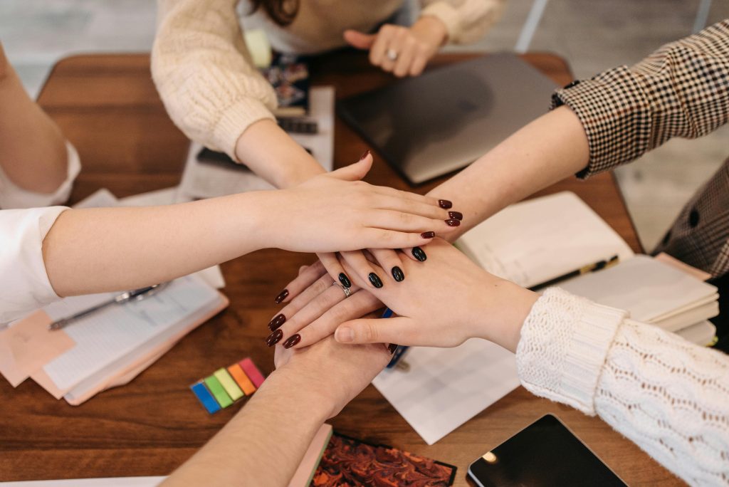 pexels-photo-6340692-6340692 Hands stacked in teamwork gesture over a table with office items symbolizing collaboration.